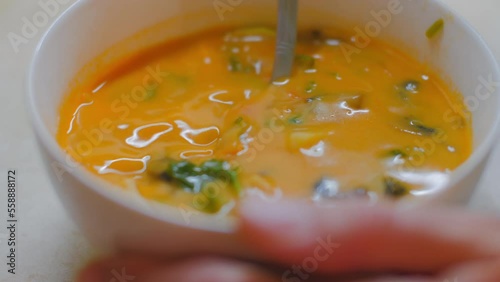 Woman stirs tasty and spicy Asian Tom Yam soup. Bright orange hot soup with meat and vegetables in porcelain bowl.