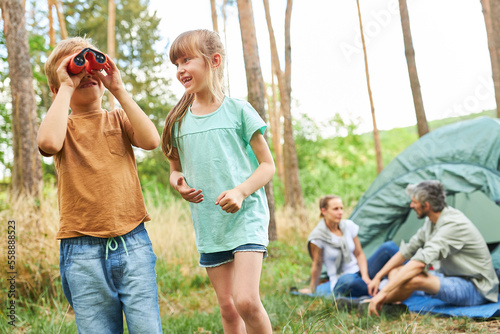 Boy looking through binoculars while camping with sister