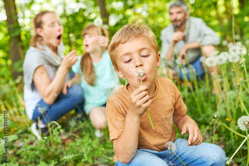 Boy blowing dandelion with family in background at forest