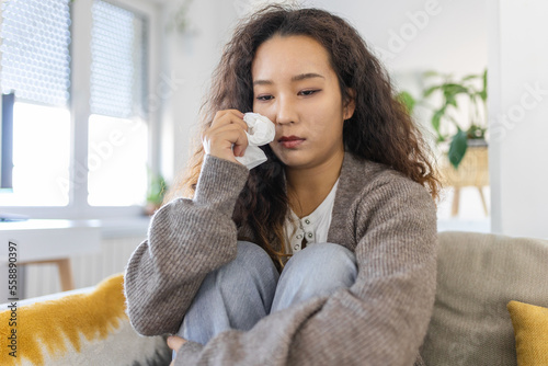 Print op canvas Unhappy young Asian woman crying alone close up, depressed girl sitting on couch