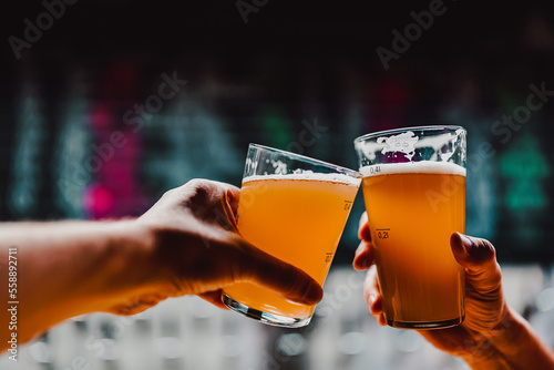 фотография Two friends hands clinking glasses of craft beer at the pub or bar