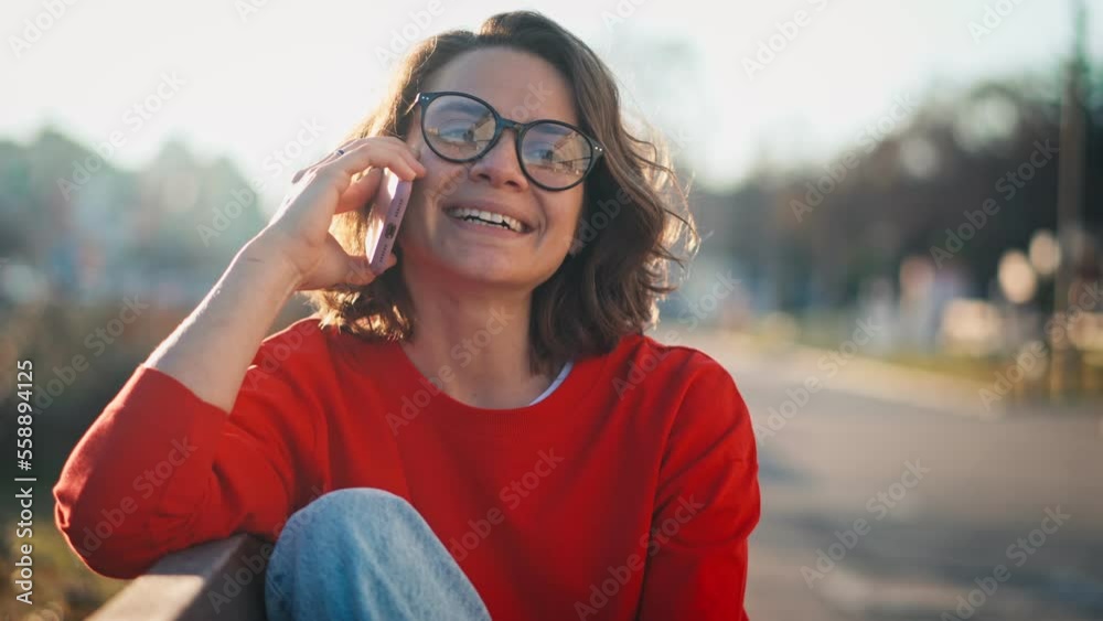 Portrait of a young caucasian cheerful woman talking on the phone while sitting on a bench in the street Portrait of a young caucasian cheerful woman talking on the phone while sitting on a bench in the street