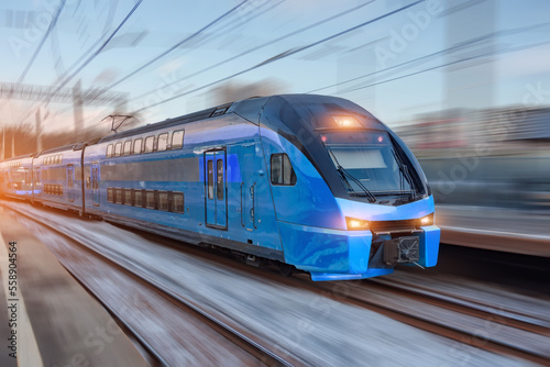 Electric passenger train drives at high speed among urban passenger station.
