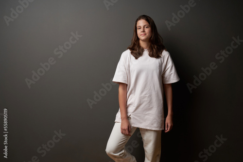 Lovely casual teen girl wearing loose fit clothes standing on dark