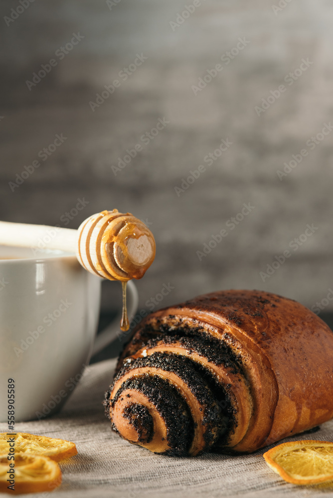 bun with poppy seeds and a cup of tea and honey on gray background bun with poppy seeds and a cup of tea and honey on gray background