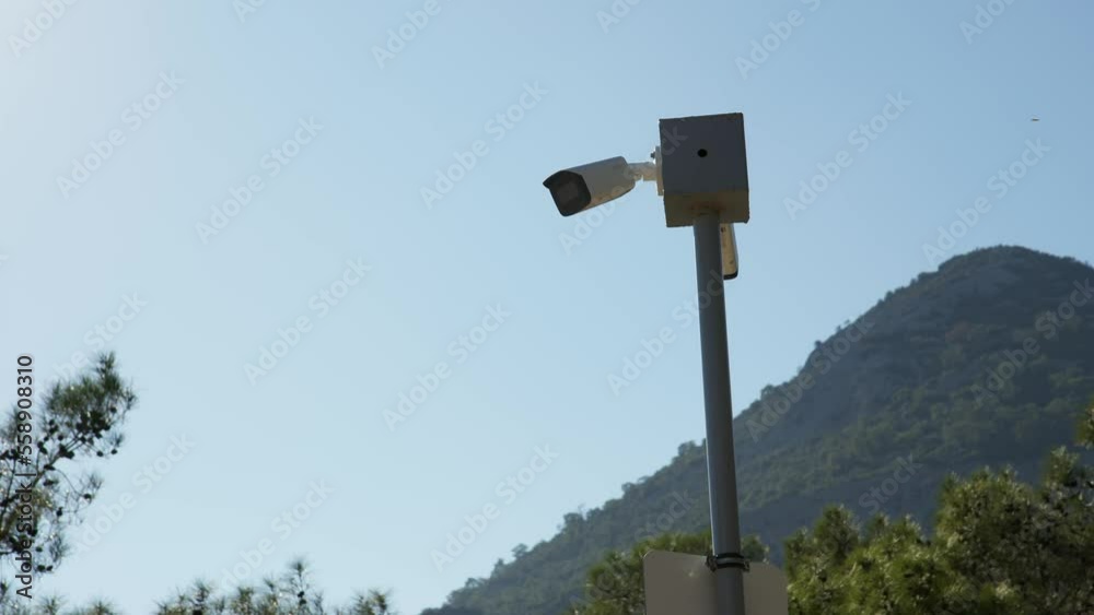 white security camera on pole in park or private area of large estate and provides round-the-clock monitoring. video camera for protection and tranquility of citizens against backdrop of mountains. white security camera on pole in park or private area of large estate and provides round-the-clock monitoring. video camera for protection and tranquility of citizens against backdrop of mountains.