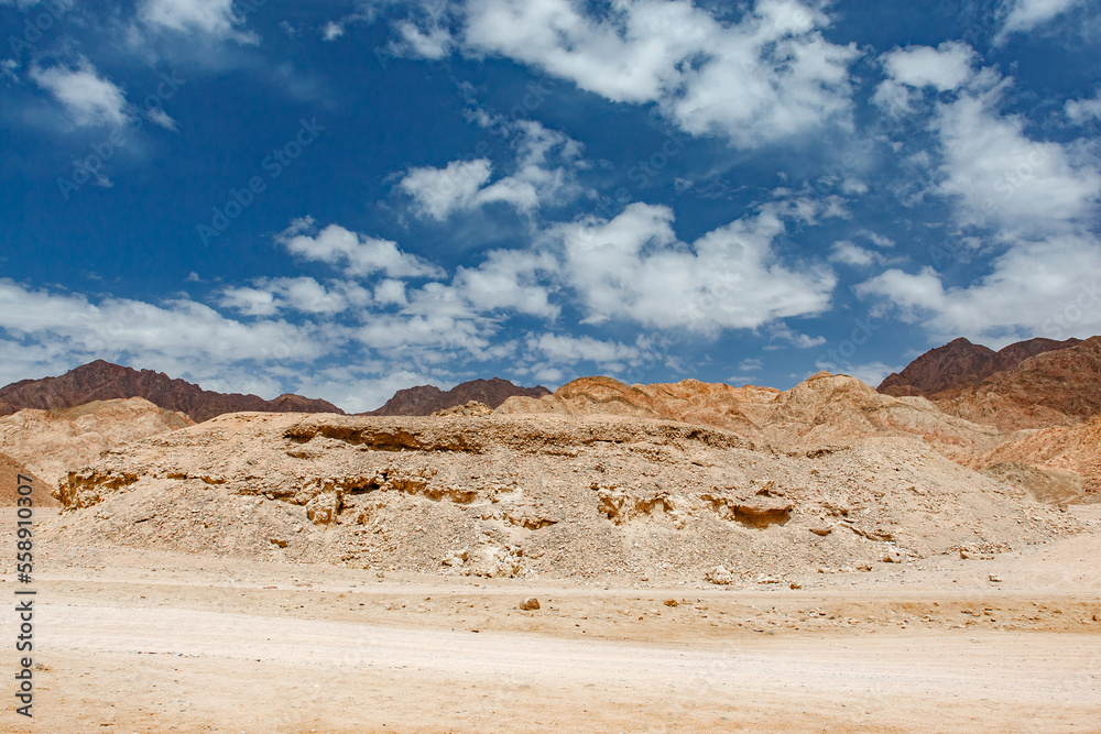 Rocky desert hills under blue sky with white clouds on clear day Rocky desert hills under blue sky with white clouds on clear day