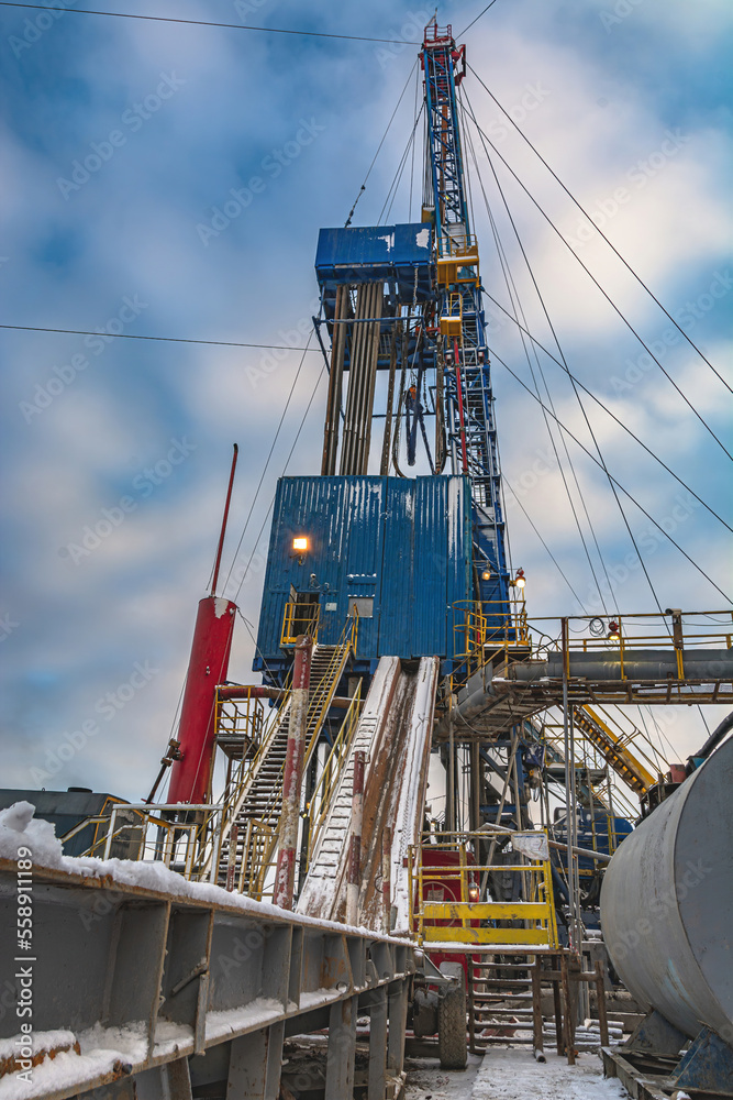 Fototapeta premium Drilling rig and drilling rig equipment for drilling oil and gas wells. Winter day. Snow lies on the structures of the installation. Blue cloudy sky