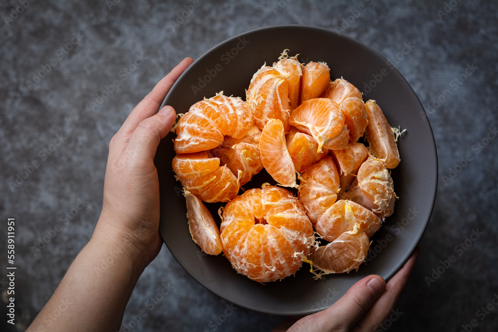 Tangerines in a bowl. The hands of a European woman hold a plate of peeled tangerines. Selective focus, dark and moody photo, shallow depth of field Tangerines in a bowl. The hands of a European woman hold a plate of peeled tangerines. Selective focus, dark and moody photo, shallow depth of field