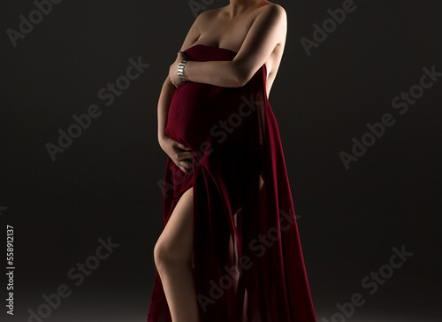 A pregnant woman in a red dress. Studio pregnancy photo shoot. Pregnancy.