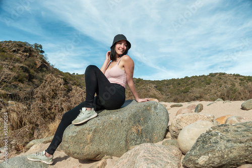beautiful tourist woman sitting on a big rock smiling and resting.