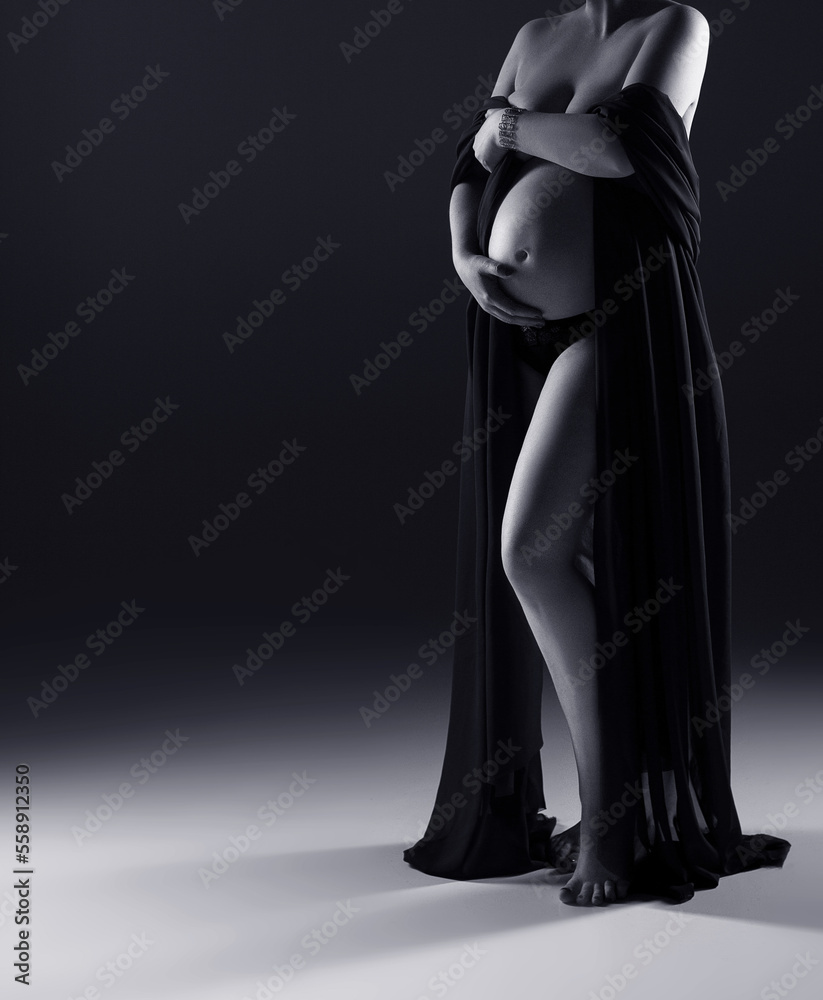 pregnant woman in black dress posing in a studio, grey background with copy space