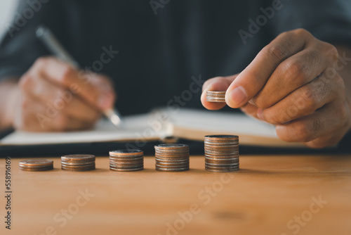 A businessman stacks coins while writing in a notebook. business success and growth. tax and financial
