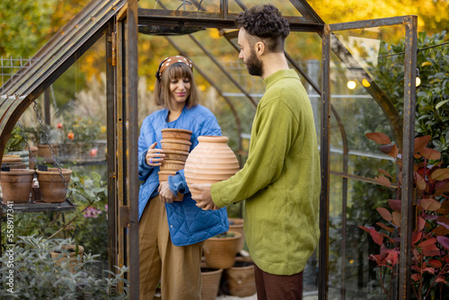 Man and woman take care of plants and flowers, gardening together in tiny orangery at backyard. Hobby or small family business of growing flowers concept photo