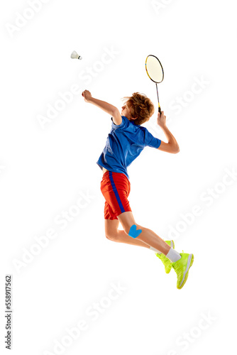 Portrait of teen boy in uniform playing badminton, serving shuttlecock with racket in a jump isolated over white background