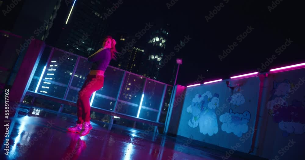 Beautiful Young Professional Female Dancer Performing an Energetic Freestyle Dance Routine on an Urban Spot with Neon Lights and Modern City Skyline with Office Skyscrapers at Night