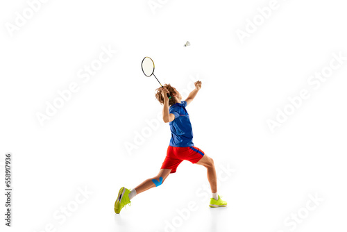 Portrait of teen boy in uniform in motion, playing badminton, serving shuttlecock with racket isolated over white background