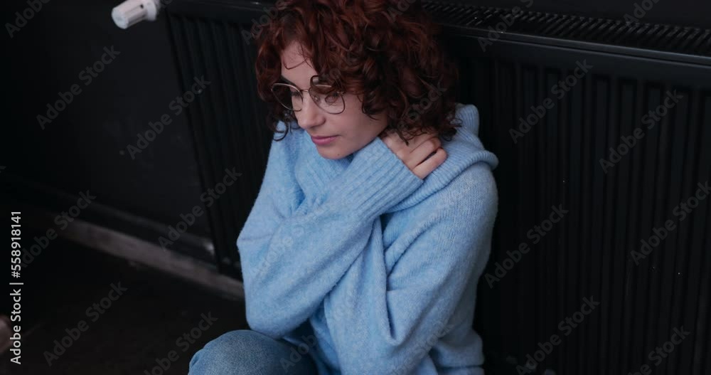 A hunched and frozen woman sits by a hot radiator. Central heating in the house. A hunched and frozen woman sits by a hot radiator. Central heating in the house.