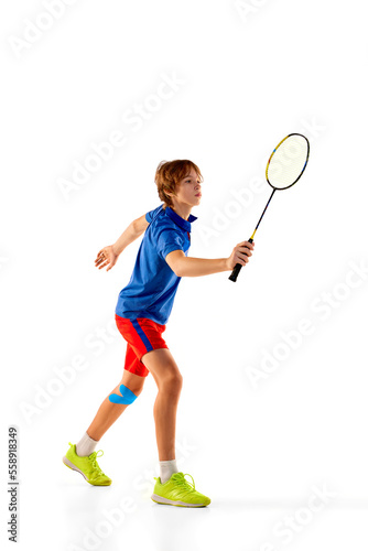 Portrait of teen boy in uniform playing badminton, training, posing with racket isolated over white background. Winner