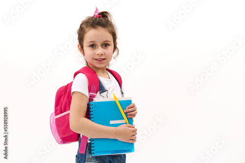 Caucasian adorable child girl, primary school student, first grader with blue copybook and pink backpack, isolated on white background. Back to school. Education and learning concept. Copy ad space