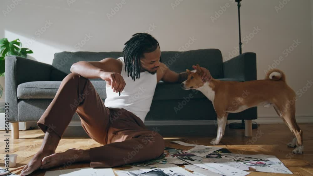Creative guy stroking dog at sofa room. Positive artist relaxing after drawing