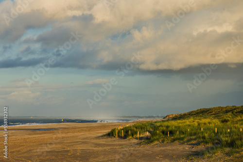 dark clouds over the sandy Northsea beach with dunes of the island of Goeree Overflakkee at sunset in winter