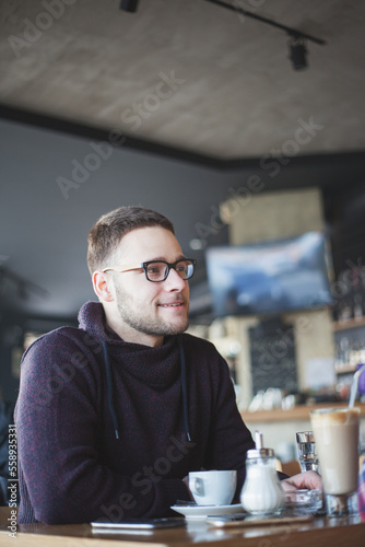 A young man is sitting alone in a cafe, drinking coffee and enjoying himself