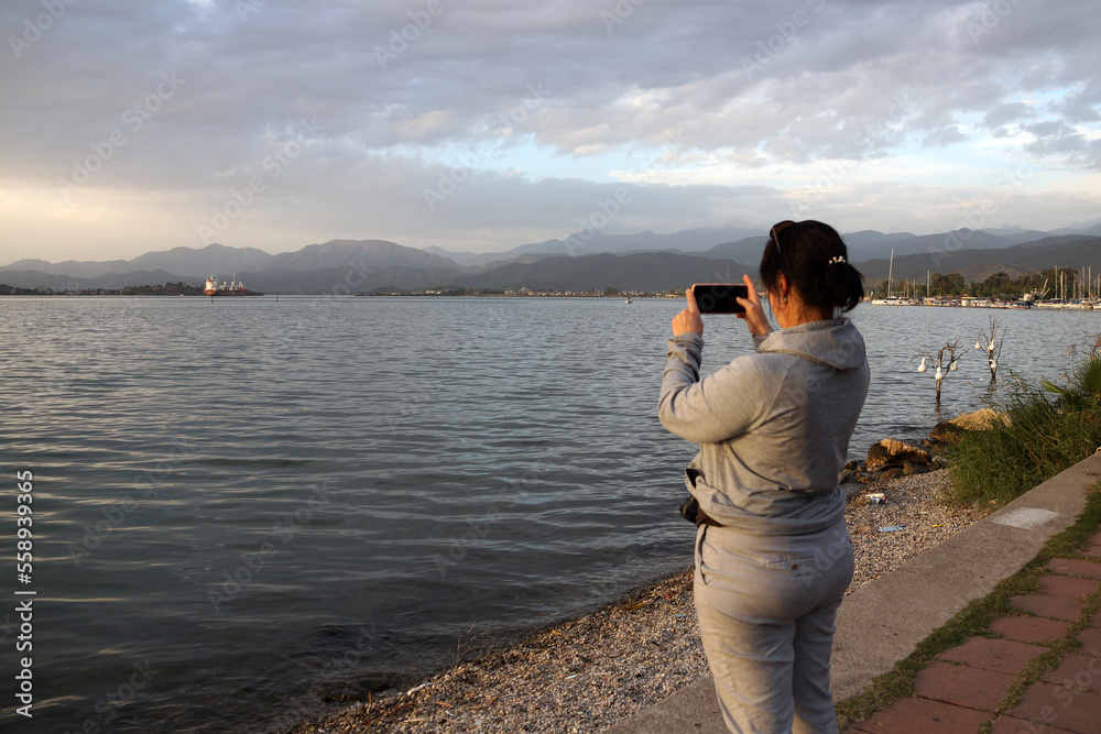 woman taking pictures on a smartphone of a cloudy sunset on the sea