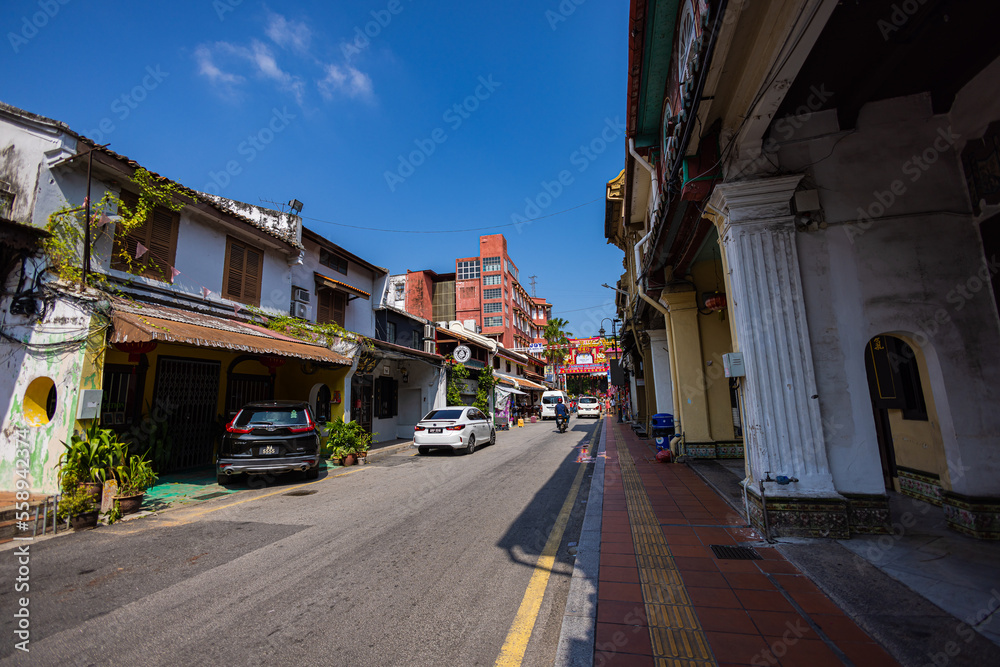 Malacca, Malaysia - August 10, 2022: The Jonker street in the center of Melaka. One of the well-known colorfully decorated and rather noisy rickshaws, occupied by tourists, drives by. Shopping street