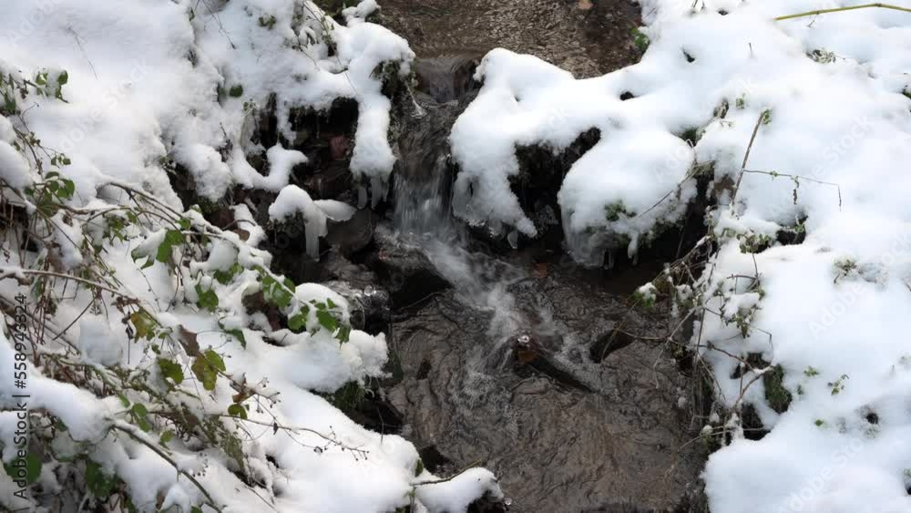 A tiny creek in winter snow as water cascades over a few rocks with icicles A tiny creek in winter snow as water cascades over a few rocks with icicles