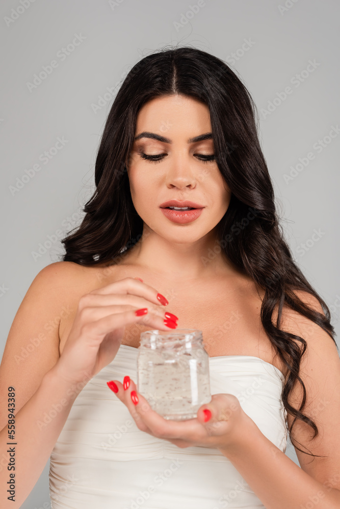 brunette woman holding jar with transparent hair gel isolated on grey. brunette woman holding jar with transparent hair gel isolated on grey.
