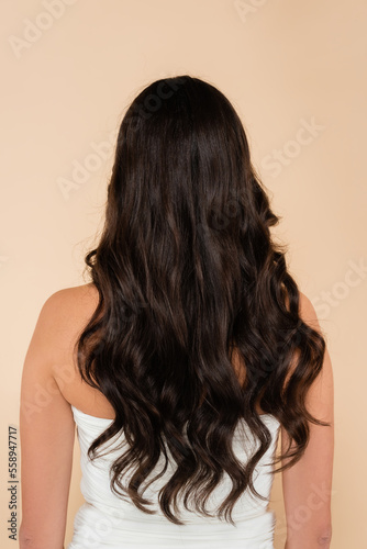 Back view of woman with wavy hair standing isolated on beige.