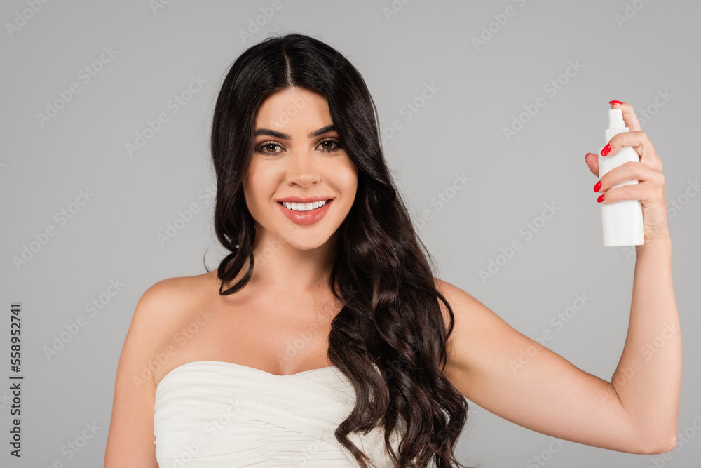 cheerful woman with shiny hair holding treatment spray bottle isolated on grey. cheerful woman with shiny hair holding treatment spray bottle isolated on grey.
