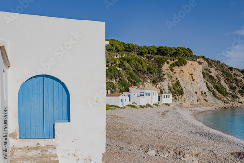 White houses with blue doors. Portitxol beach, Cala Barraca in the Autonomous Community of Valencia, Alicante, Spain. White stone beach.