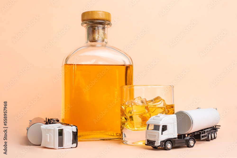 Bottle and glass of whiskey next to two toy tankers, one of them overturned, incompatibility of professional driving and alcohol. Bottle and glass of whiskey next to two toy tankers, one of them overturned, incompatibility of professional driving and alcohol.