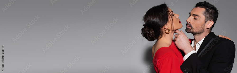 Bearded man in suit touching neck of sensual girlfriend on grey background, banner. Bearded man in suit touching neck of sensual girlfriend on grey background, banner.