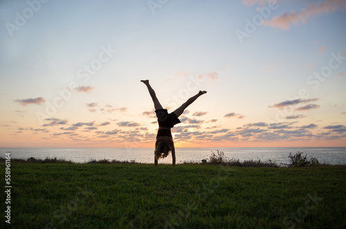 slender girl teenager makes flip on hands upside down at sunset   beautiful silhouette. concept of cheerfulness  sports education  healthy lifestyle. young woman trains with pleasure. photo in motion