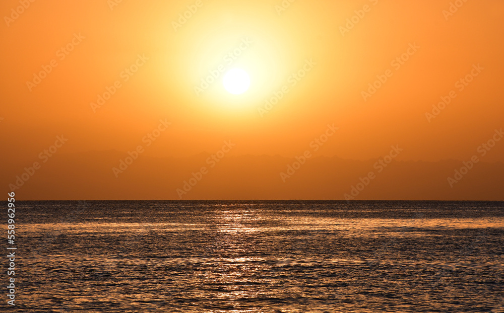 Sunrise over the sea. The bright yellow-gold color of the sky. The glare of the sun and a slight ripples on the surface of the water. A beautiful start to the day
