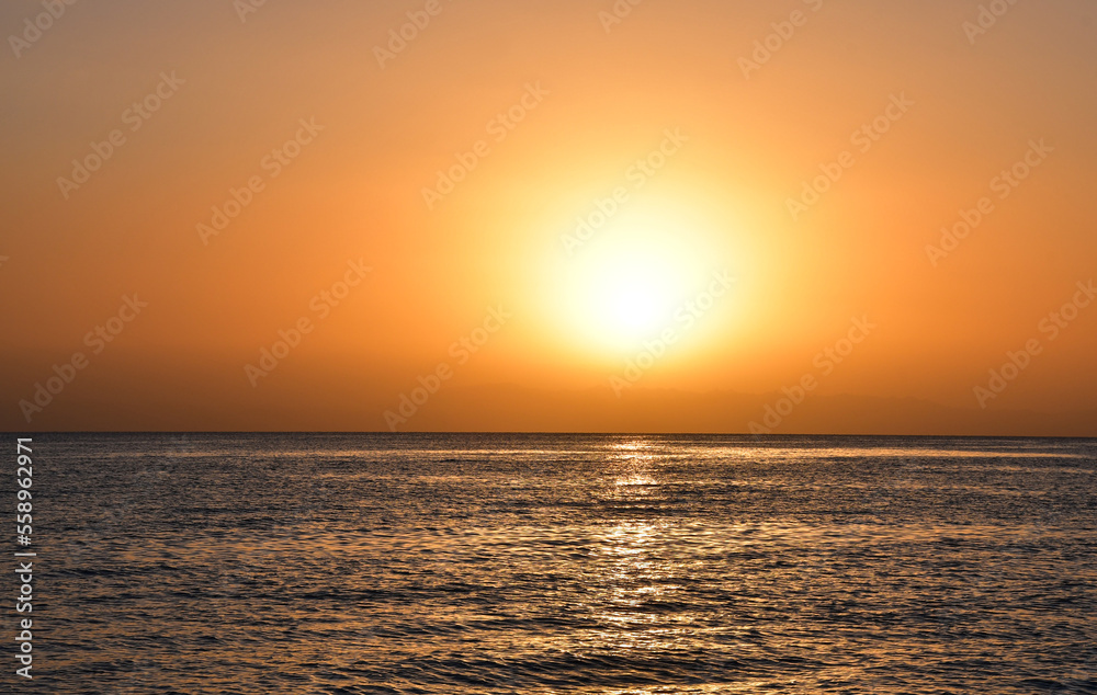 Sunrise over the sea. The bright yellow-gold color of the sky. The glare of the sun and a slight ripples on the surface of the water. A beautiful start to the day
