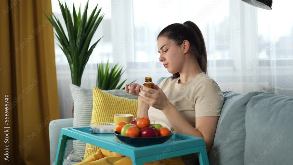 Young woman supporting her immune system with good supplements and plenty of organic fruits. Sitting on a couch and drinking medicine with a cup of herbal tea. Young woman supporting her immune system with good supplements and plenty of organic fruits. Sitting on a couch and drinking medicine with a cup of herbal tea.