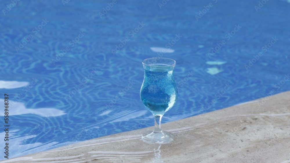 blue lagoon cocktail liquid in glass on swimming pool edge shore blue water waterfall stairs steps in background slow motion or 4k.summer vacation waves hotel building sea beach relax drink alcohol blue lagoon cocktail liquid in glass on swimming pool edge shore blue water waterfall stairs steps in background slow motion or 4k.summer vacation waves hotel building sea beach relax drink alcohol