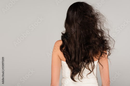 back view of brunette woman with long and tousled hair isolated on grey.