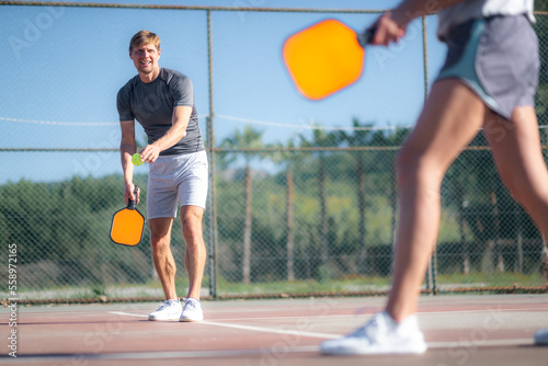 couple playing pickleball game, hitting pickleball yellow ball with paddle, outdoor sport leisure activity.