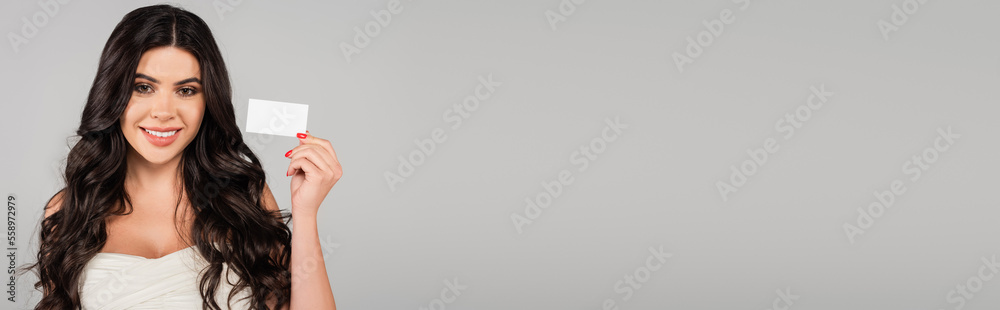 happy and brunette woman with shiny hair holding blank card isolated on grey, banner. happy and brunette woman with shiny hair holding blank card isolated on grey, banner.
