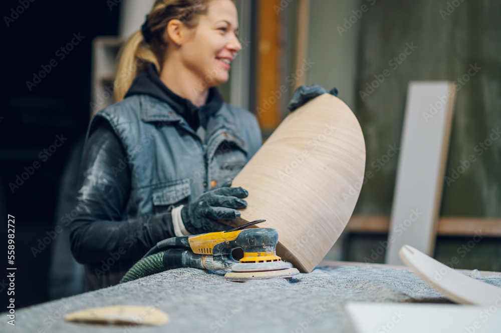 Woman carpenter using an electric sander in a workshop or factory Woman carpenter using an electric sander in a workshop or factory
