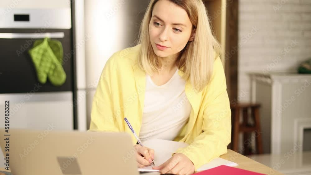 Attractive young blond girl preparing for exam and studying at home Charming young student focused on learning and make notes in her notebook and looking at the camera indoors Attractive young blond girl preparing for exam and studying at home Charming young student focused on learning and make notes in her notebook and looking at the camera indoors
