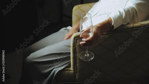 Woman holding glass with champagne sitting on armchair in her room. Close-up pretty woman relaxes with a glass of chapagne. photo