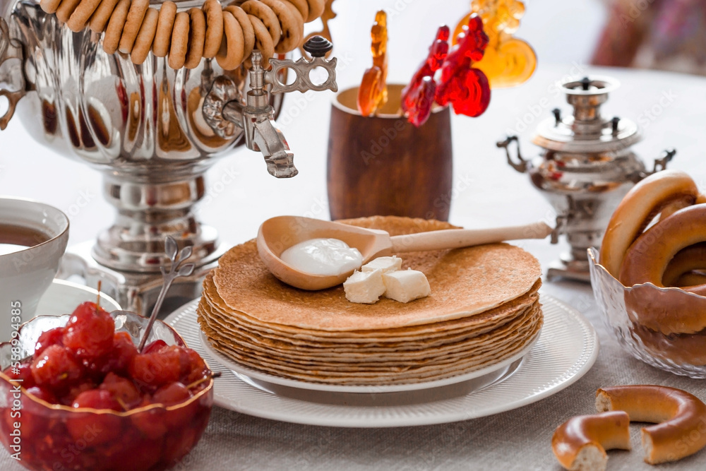 Russian traditions. Russian holiday Maslenitsa. Still life with a cup of tea, a stack of pancakes, sour cream, honey, cubes of butter, bagels, dried fruits, caramel cockerel and samovars.