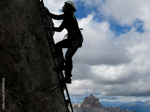 Rock climber on a rock with clouds background. Woman reaching the top of rock in Dolomites mountain.