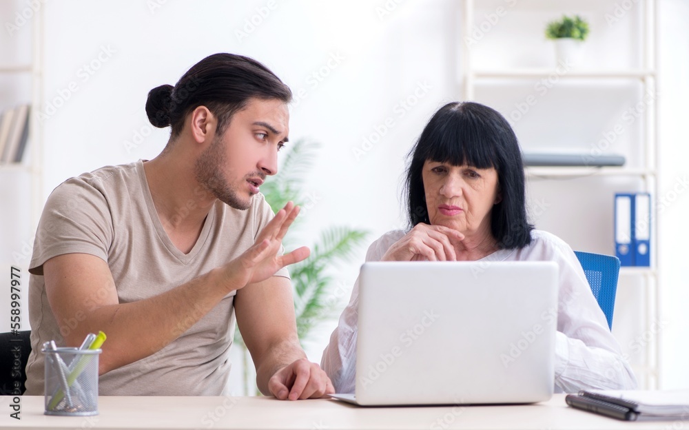 Young male employee explaining to old female colleague how to us Young male employee explaining to old female colleague how to us